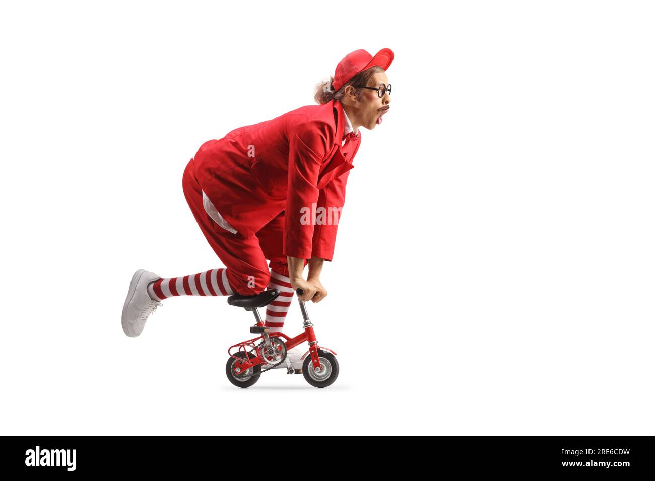 Funny entertainer in a red suit riding a small bike isolated on white background Stock Photo