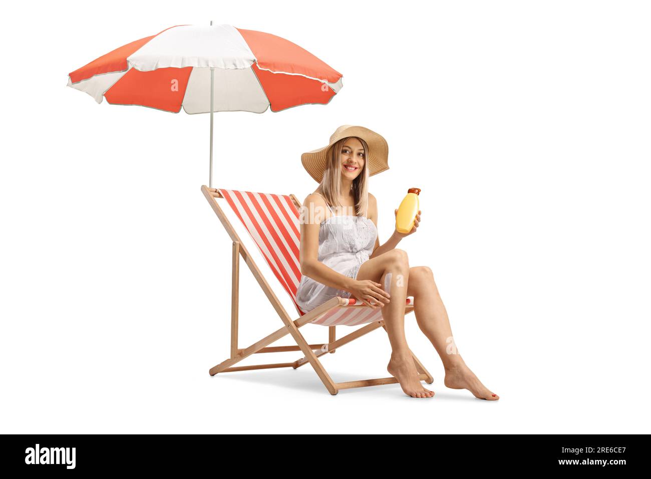 Woman sitting on a deck chair and applying sun cream on legs isolated on white background Stock Photo