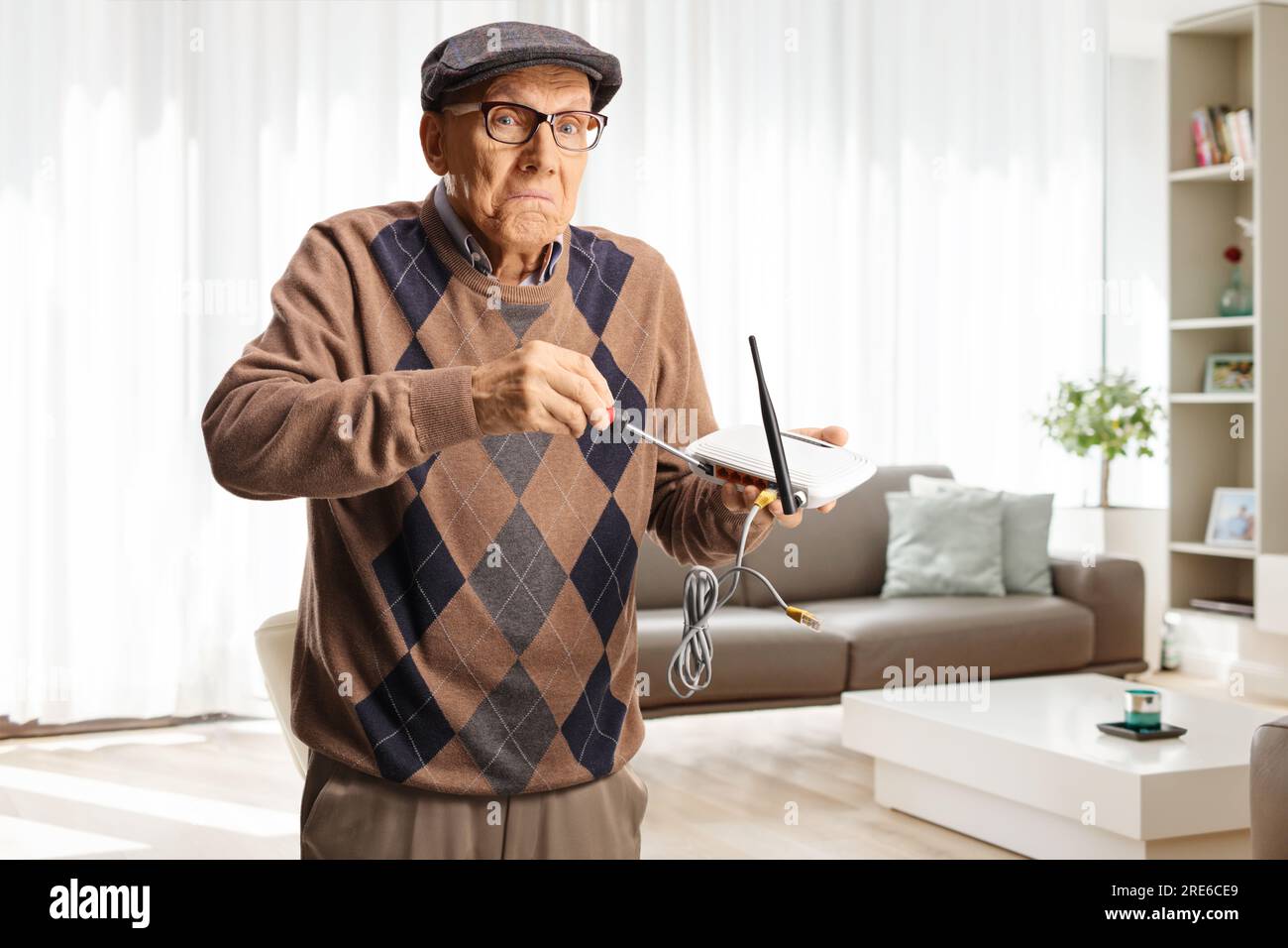 Funny old man fixing a router with a screwdriver at home in a living room Stock Photo