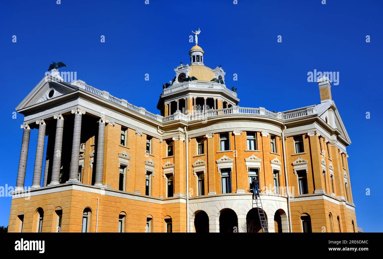 Harrison County Courthouse in Marshall, Texas receives a facelift.  Worker standing on a tall ladder repaints the trim on upper story windows. Stock Photo
