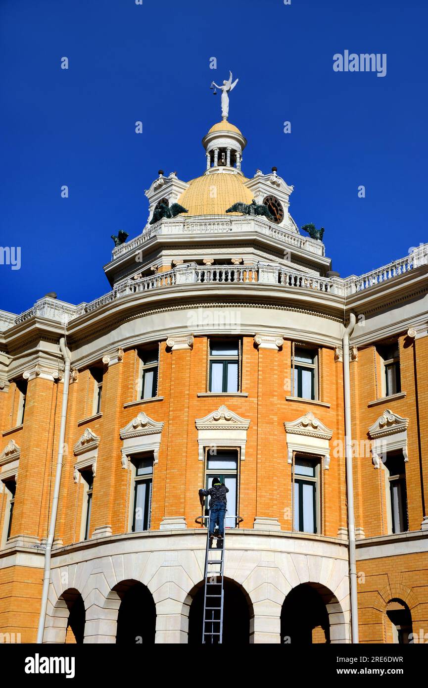 man repaints the green trim on the Harrison County Courthouse in Marshall, Texas.  He is standing on an extension ladder on a sunny day. Stock Photo