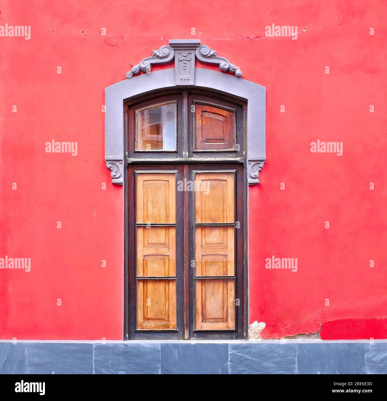 A joyful wooden window frame in a bright red wall, a lovely example of classic European style architecture. Stock Photo