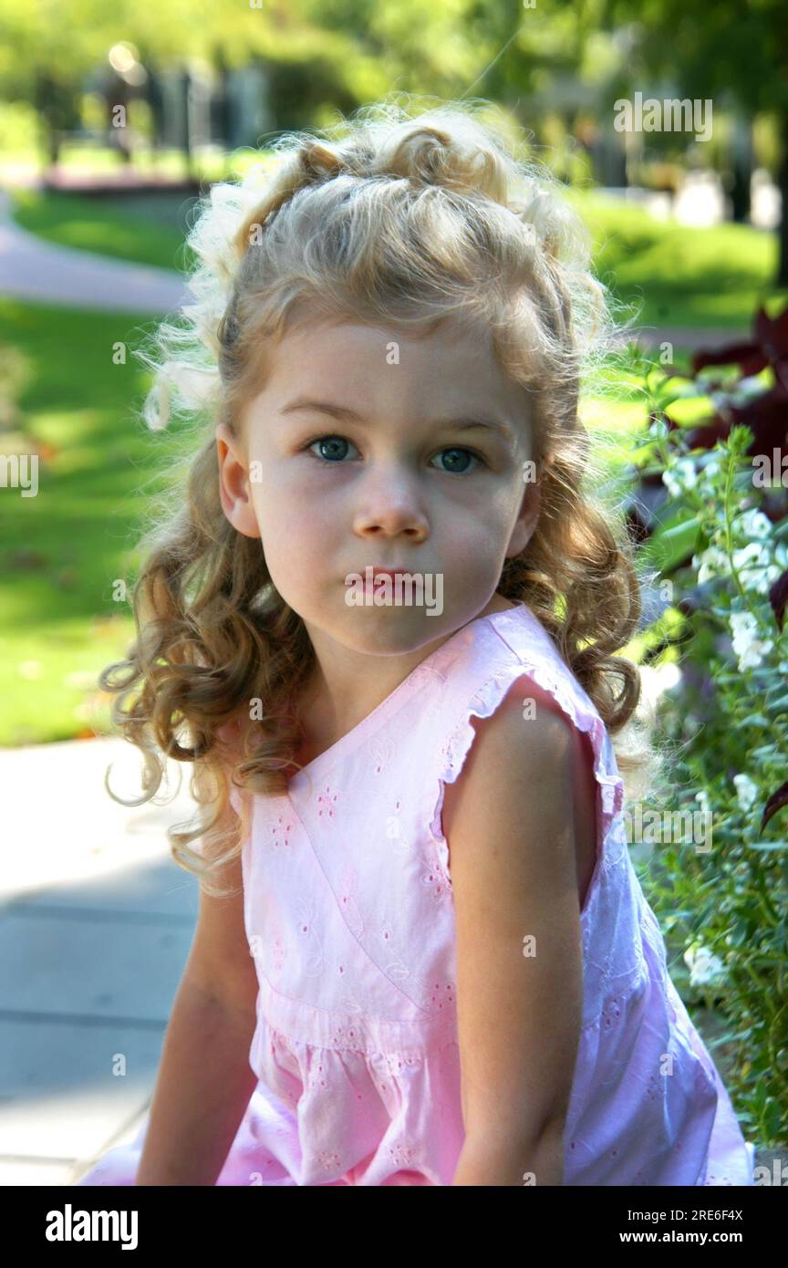 Angelic little girl looks into the camera.  She is thinking and looking off into the distance.  She has blond hair and ringlets. Stock Photo