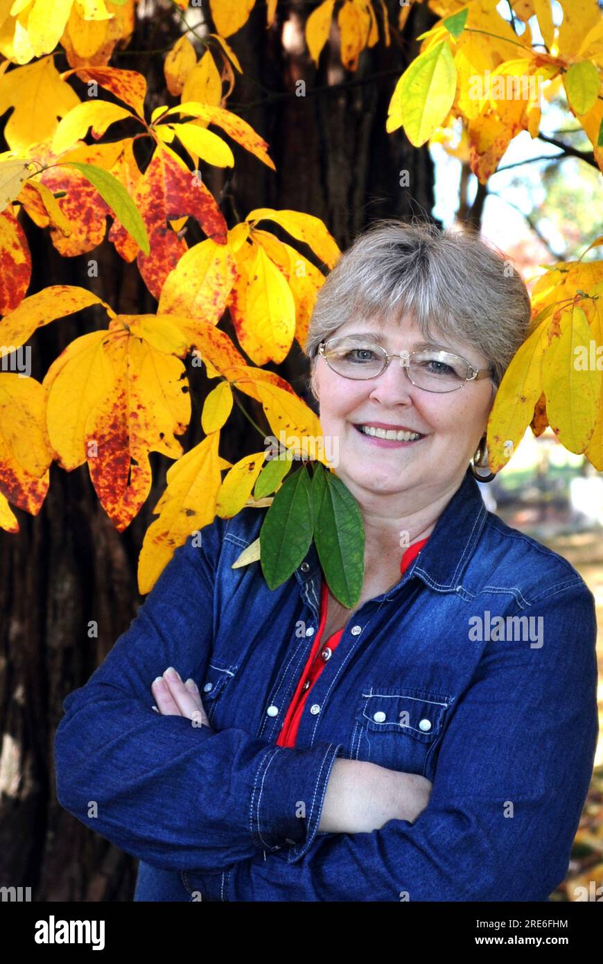 Mature woman stands with her face framed by yellow Fall leaves, and