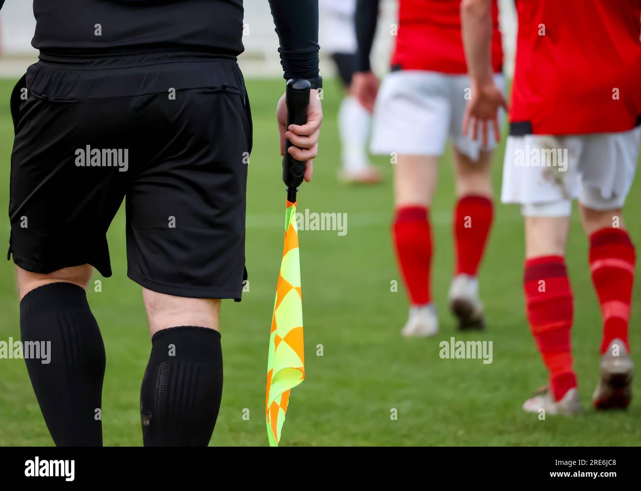 Association football referee's assistant o soccer linesman holding checkered flag on touchline during football game football players in background.. Stock Photo