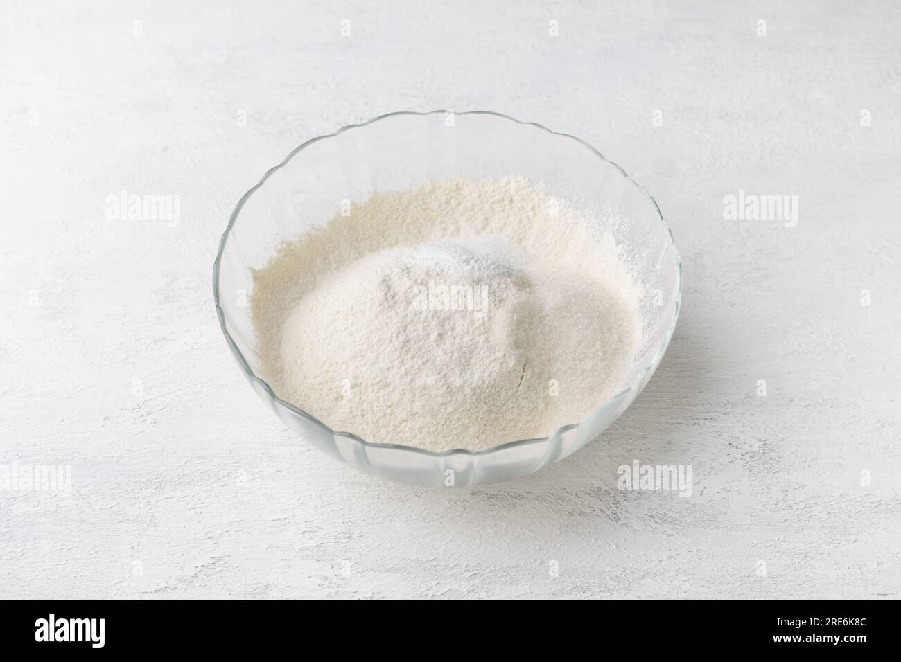 Glass bowl with sifted flour, sugar and baking powder on a light gray background. Cooking delicious homemade pastry step by step. Stock Photo