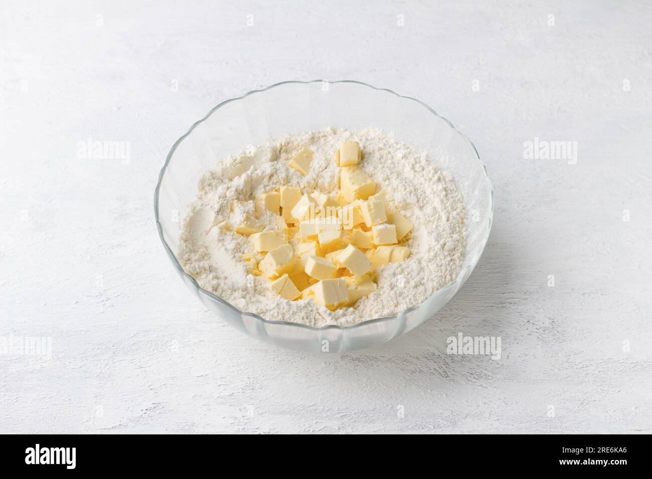 Glass bowl with flour and butter cubes on a light gray background. Cooking delicious homemade cakes step by step. Stock Photo