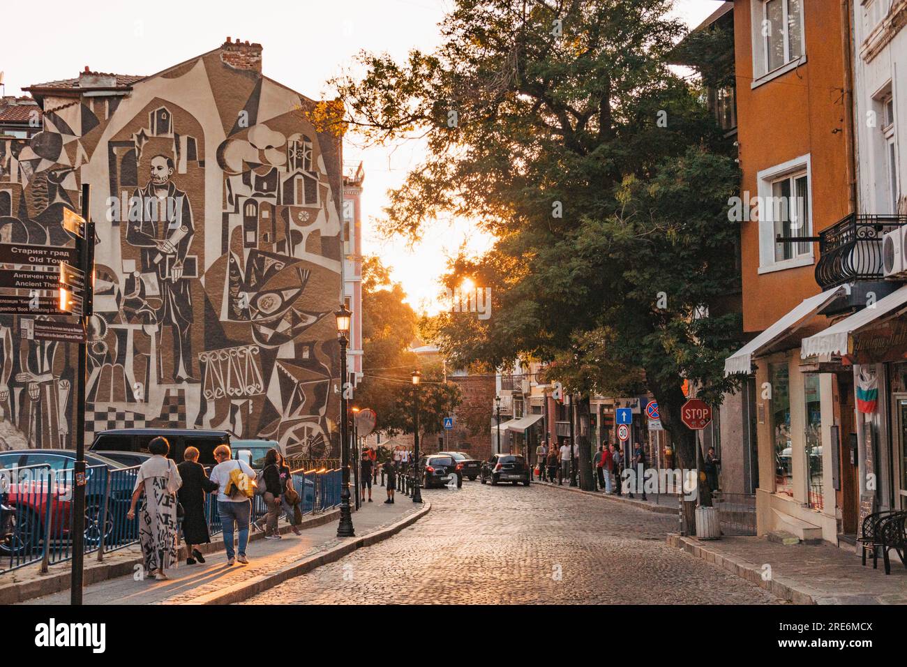 sun sets down an old town street in Plovdiv, Bulgaria. Featuring a large mural on the side of an apartment Stock Photo