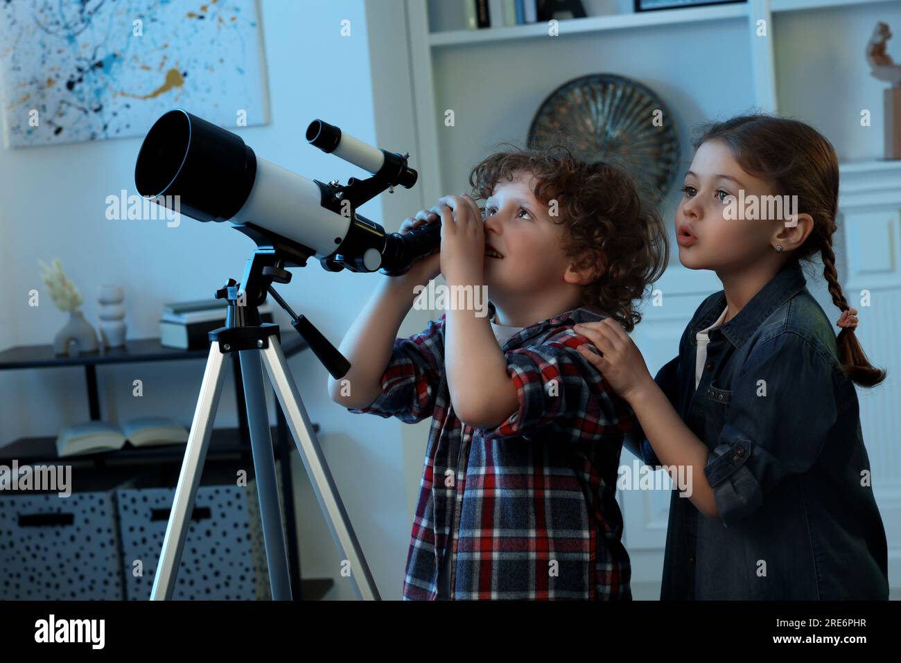 Cute little children using telescope to look at stars in room Stock