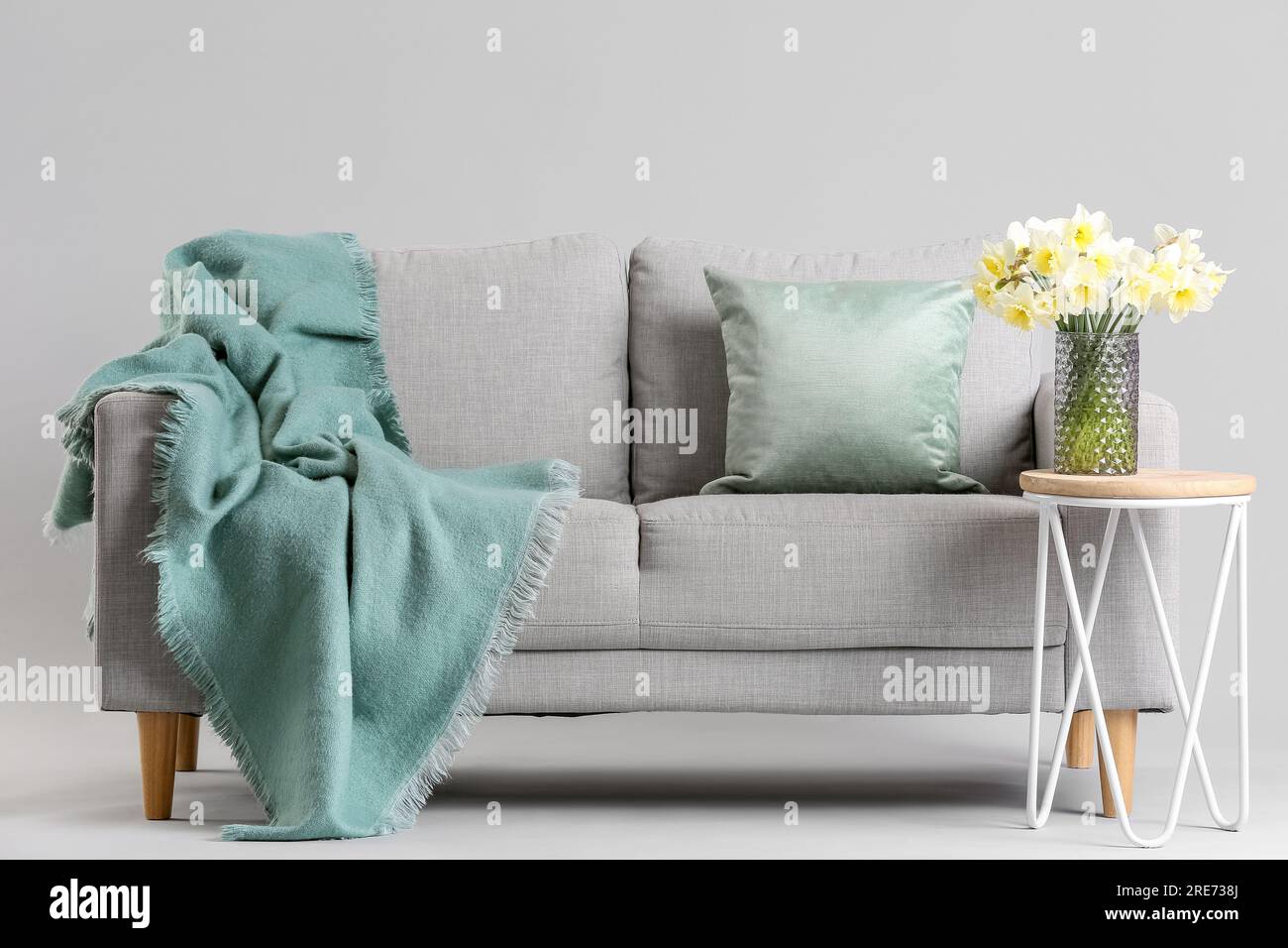 Cozy sofa and coffee table with narcissus flowers in vase on grey ...
