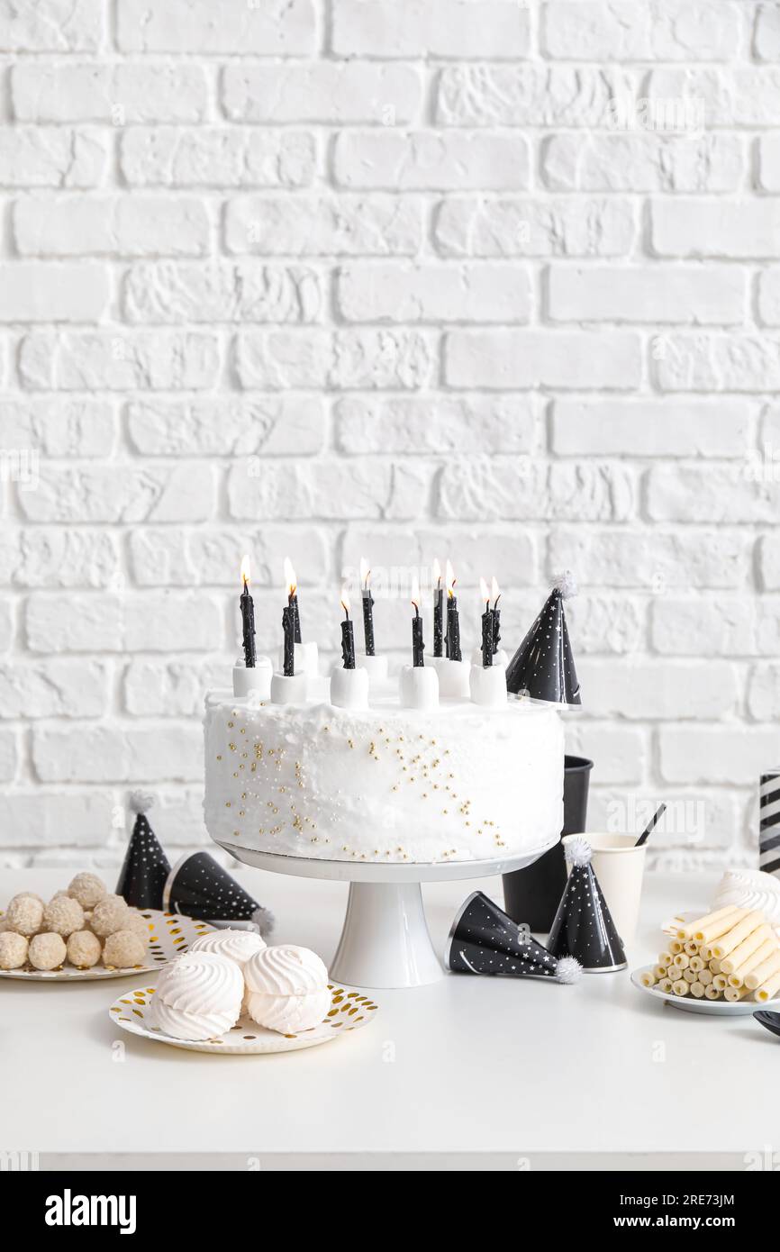 Birthday cake with candles and sweets on white table near brick wall ...