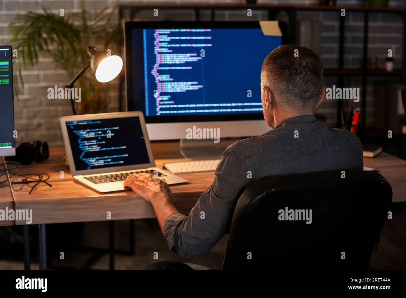 Mature male programmer working in office at night, back view Stock Photo