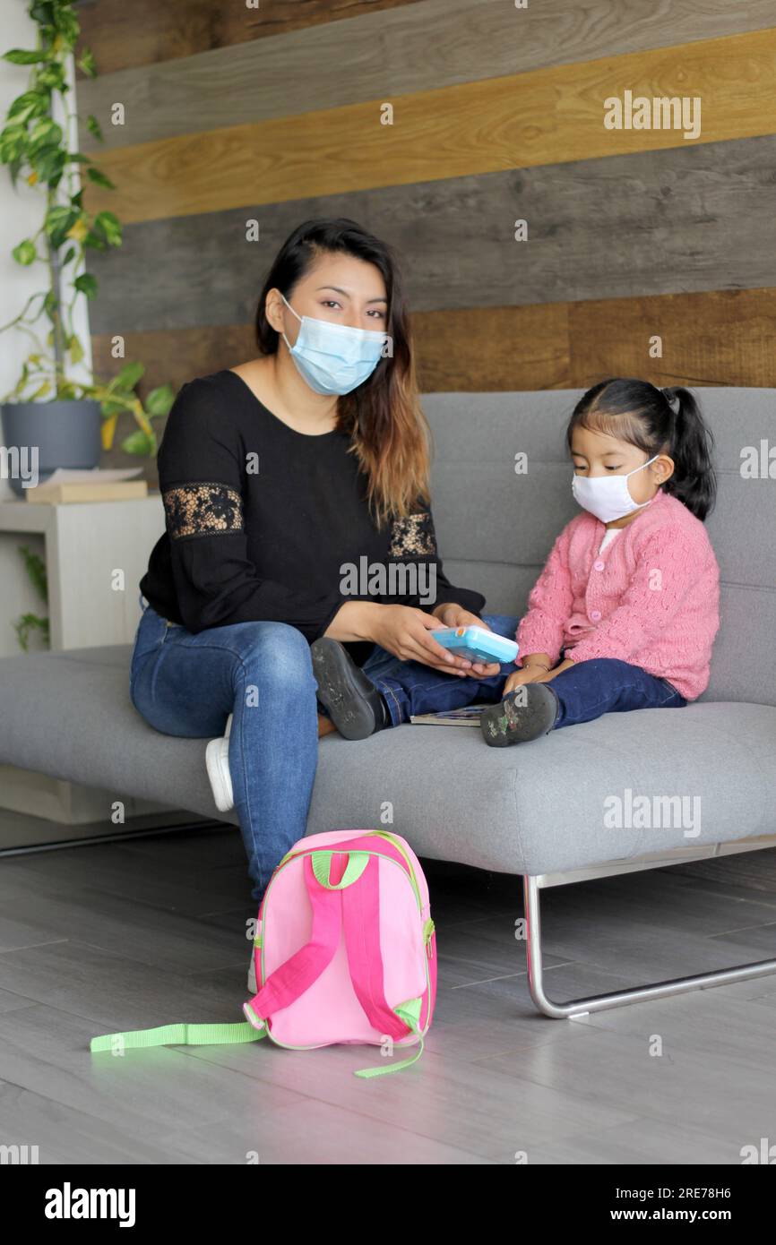Latin mom and 3 year old girl with protective face masks and backpack for back to school, new normal covid-19 Stock Photo