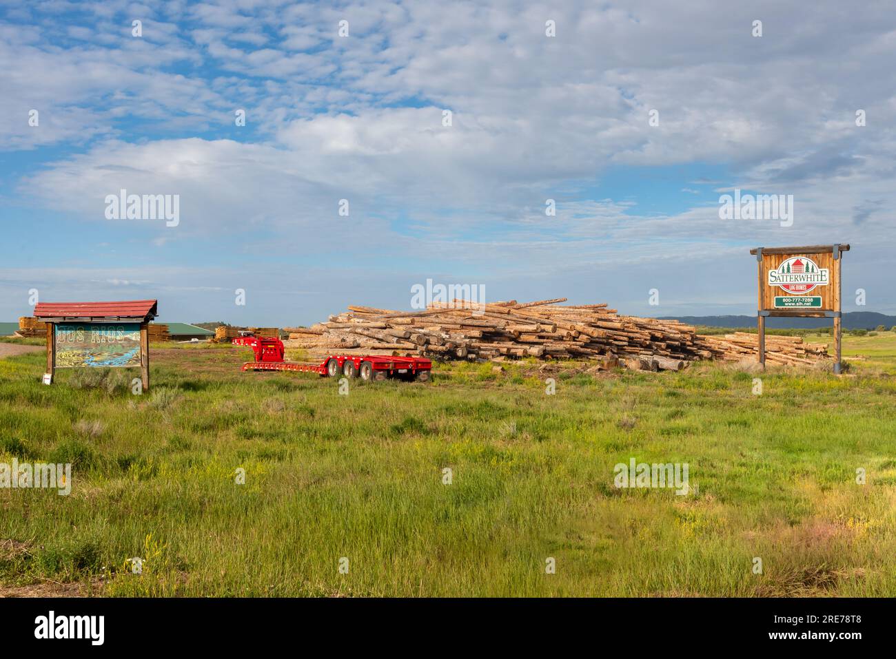 Large pile of logs to build homes, two signs read Satterwhite Log Homes