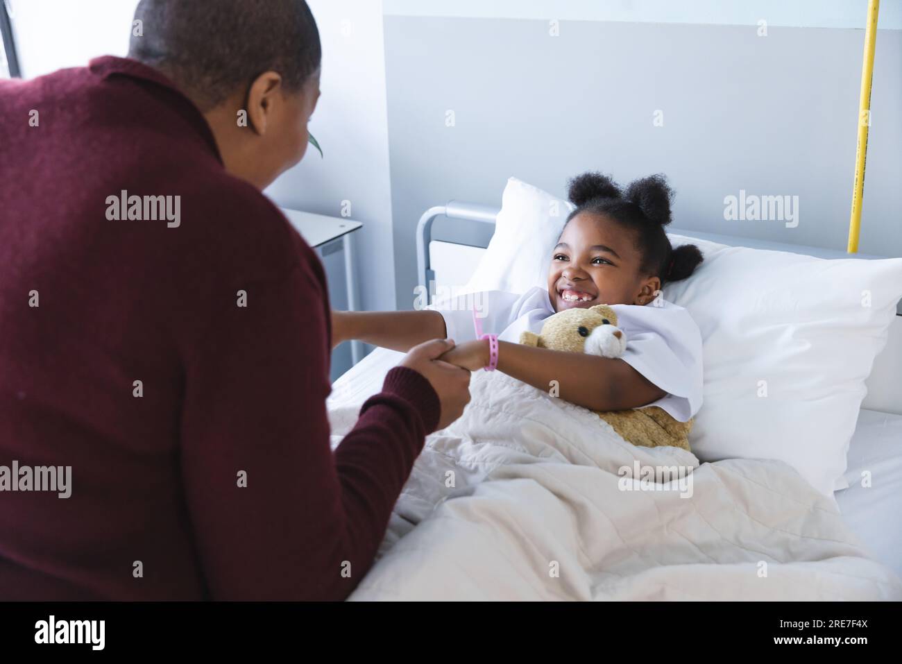 African american girl patient lying on bed holding hands with her mother in patient room at hospital Stock Photo