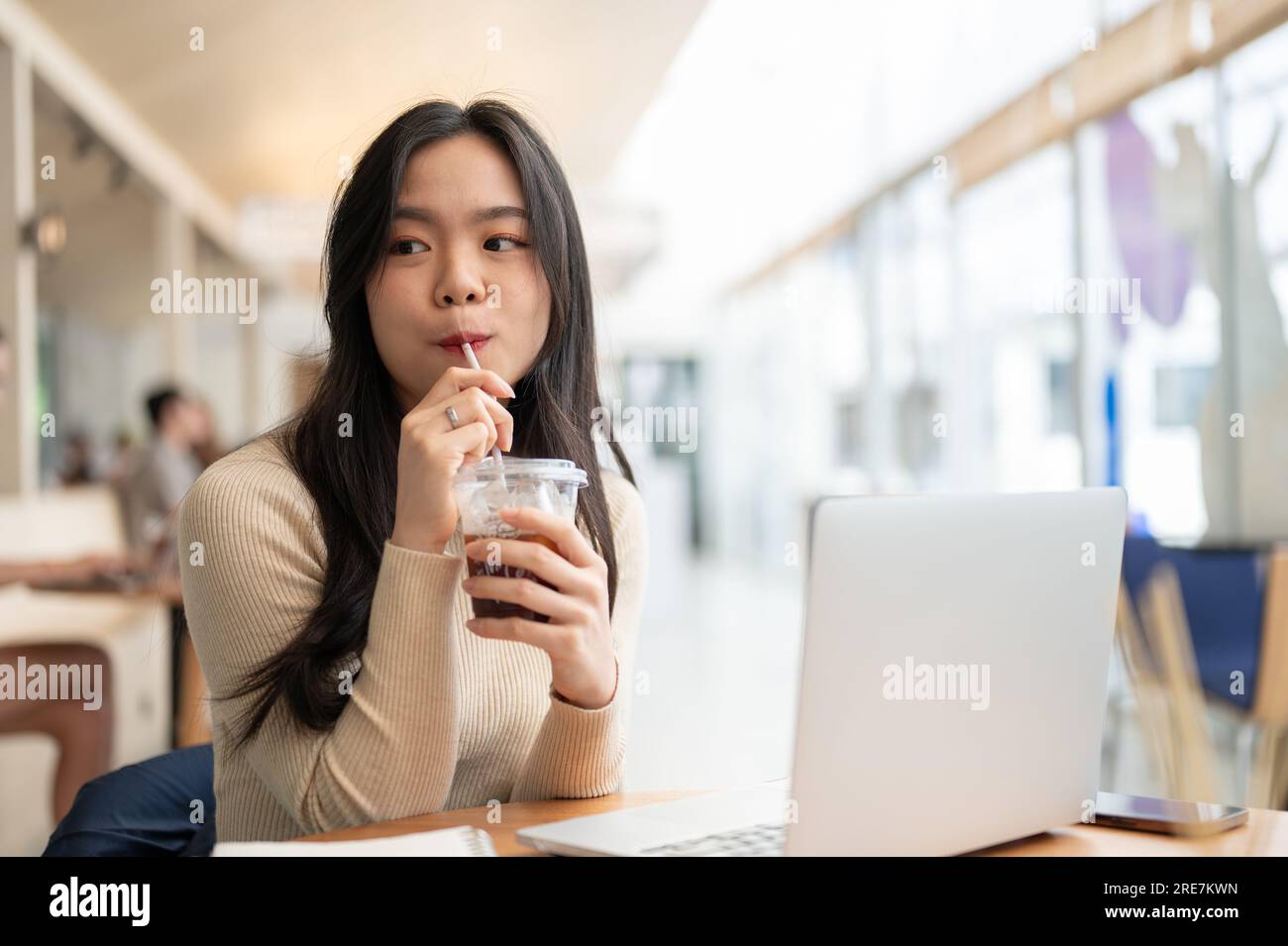 A happy and charming young Asian woman enjoying her iced coffee while ...