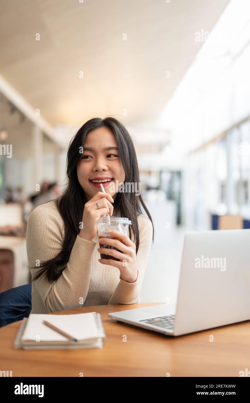 A portrait of a happy and charming young Asian woman enjoying her iced ...
