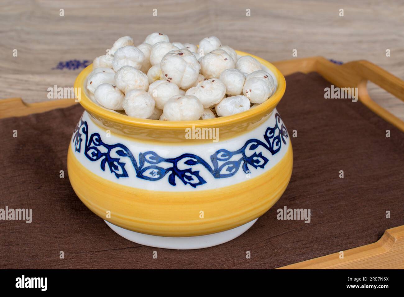 Makhana or foxnut in beautiful yellow and blue pot on a wooden tray. selective focus on subject Stock Photo