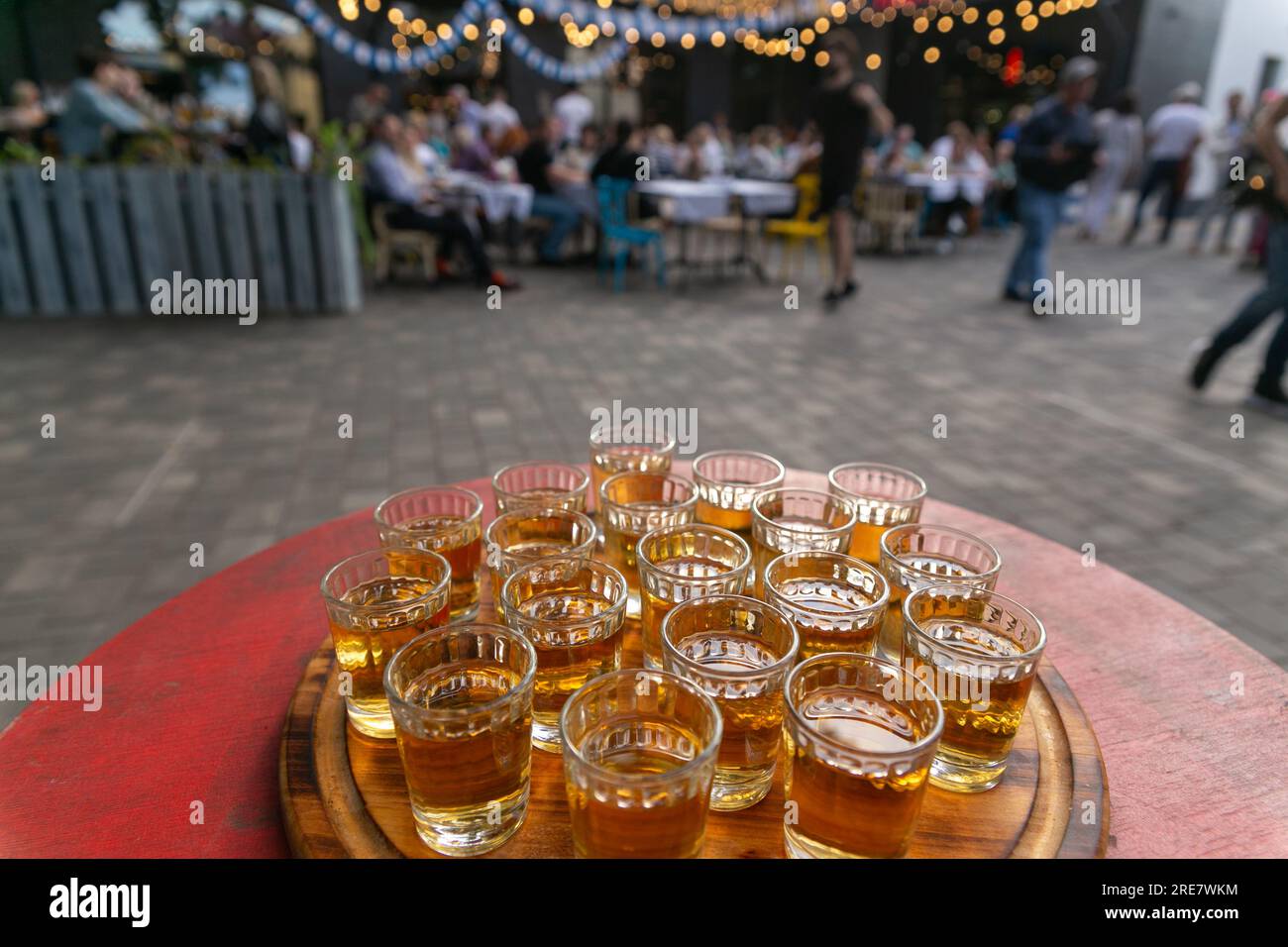 Small glasses filled with brandy on a wooden tray. Alcoholic buffet in street cafe. Shots with alcoholic beverage for taste. Stock Photo