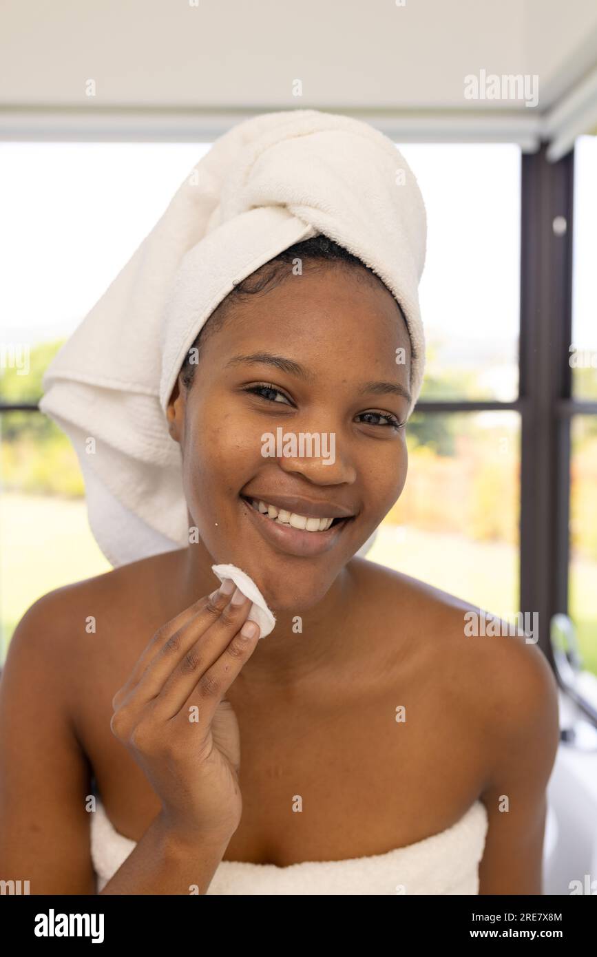 African american woman wearing towel on head cleansing face and looking