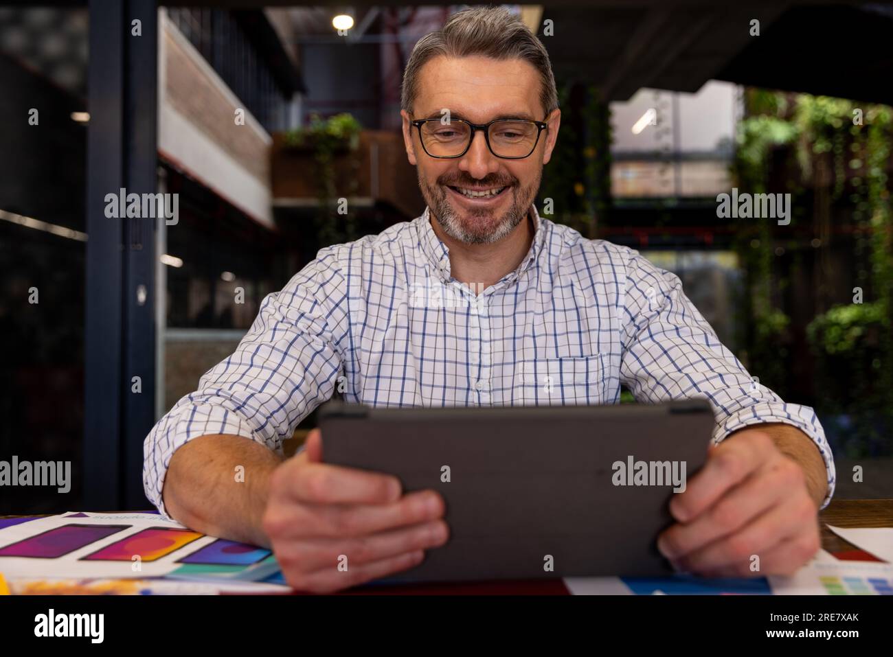 Caucasian businessman smiling while using a digital tablet at modern office Stock Photo