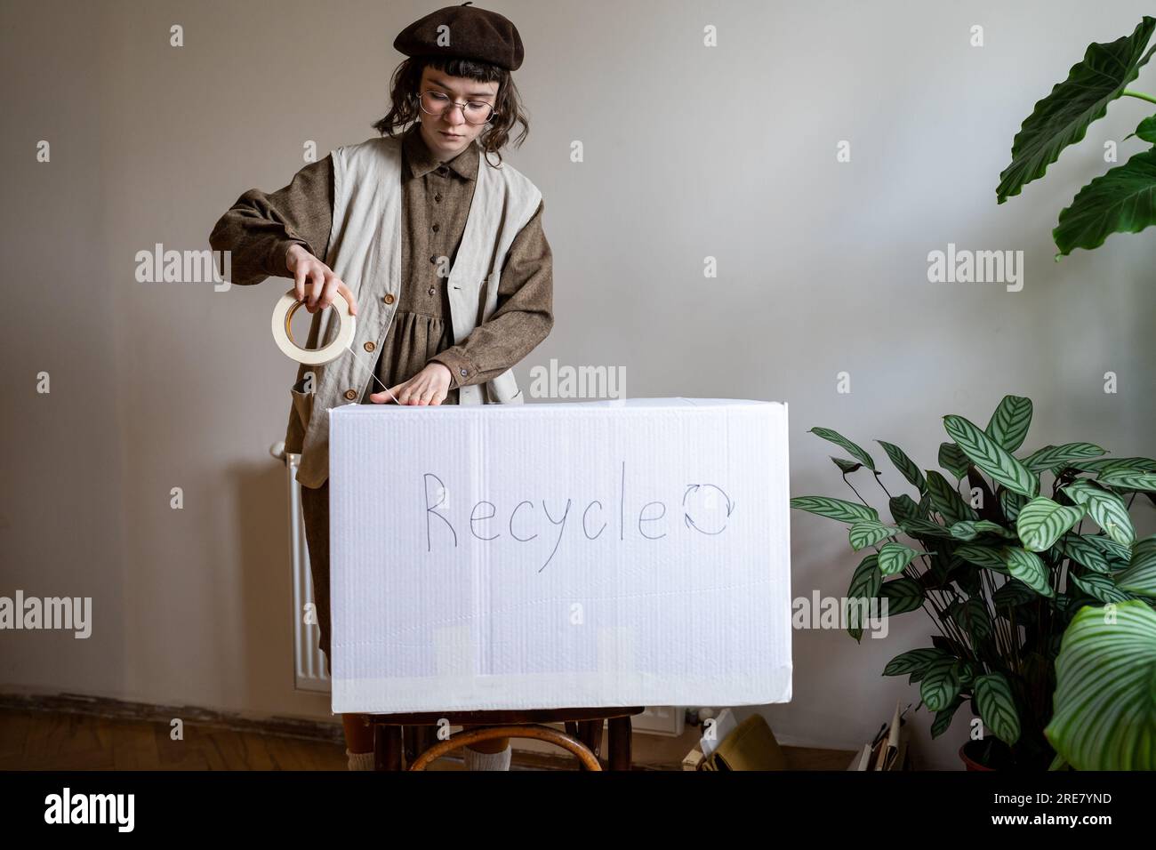 Eco activist standing at home holding scotch tape packing old clothes in cardboard box for recycling Stock Photo