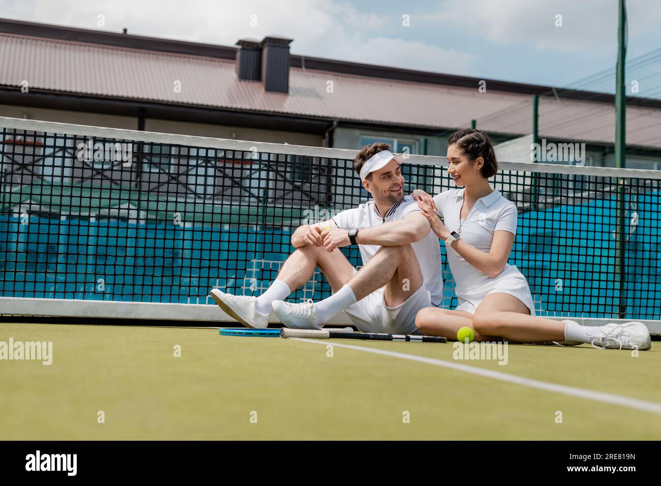 healthy lifestyle, cheerful man and woman sitting near tennis net, racket and ball, positivity Stock Photo