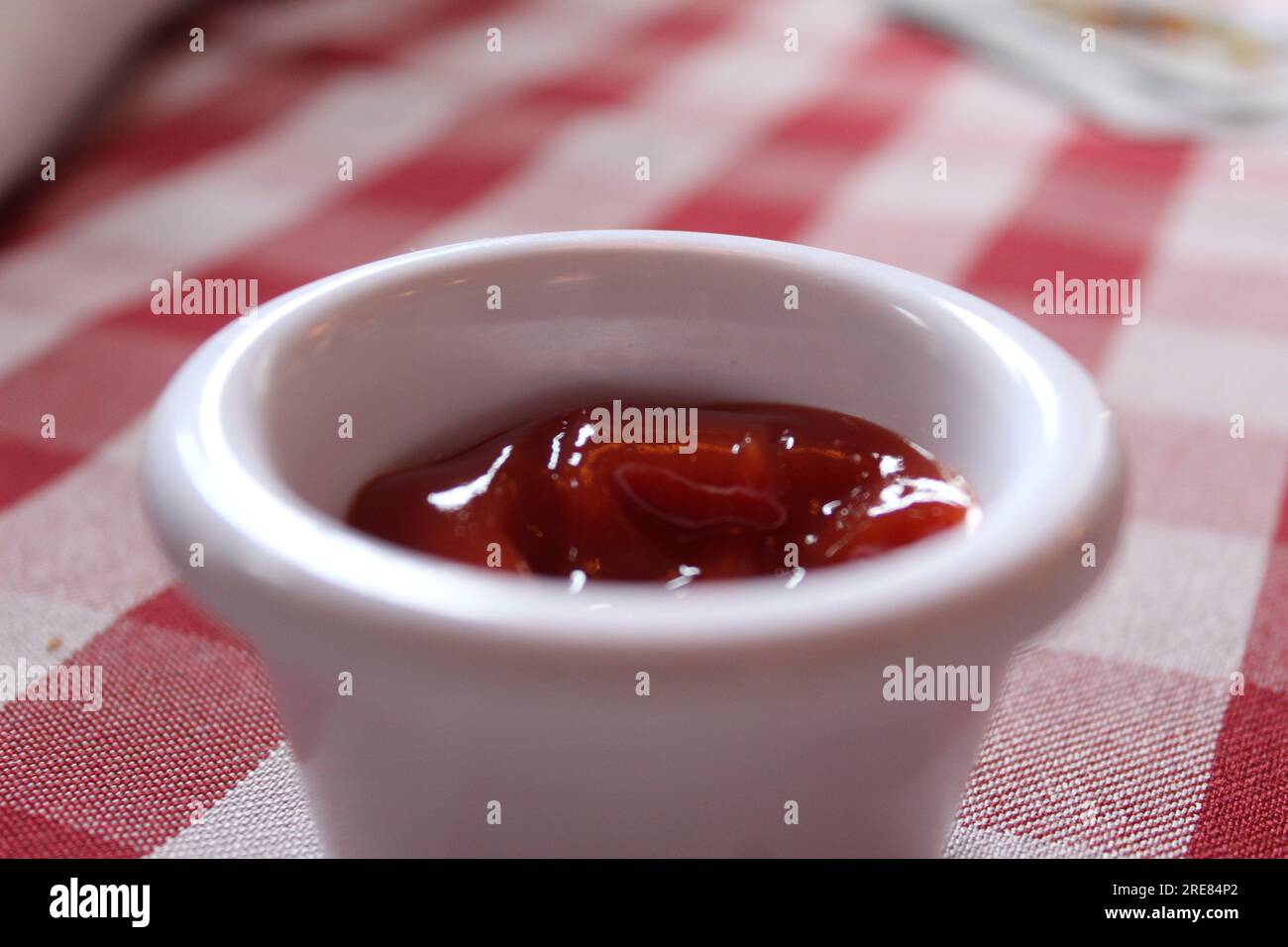 A close up photo of a small pot of tomato ketchup on a red and white checkered table. Stock Photo
