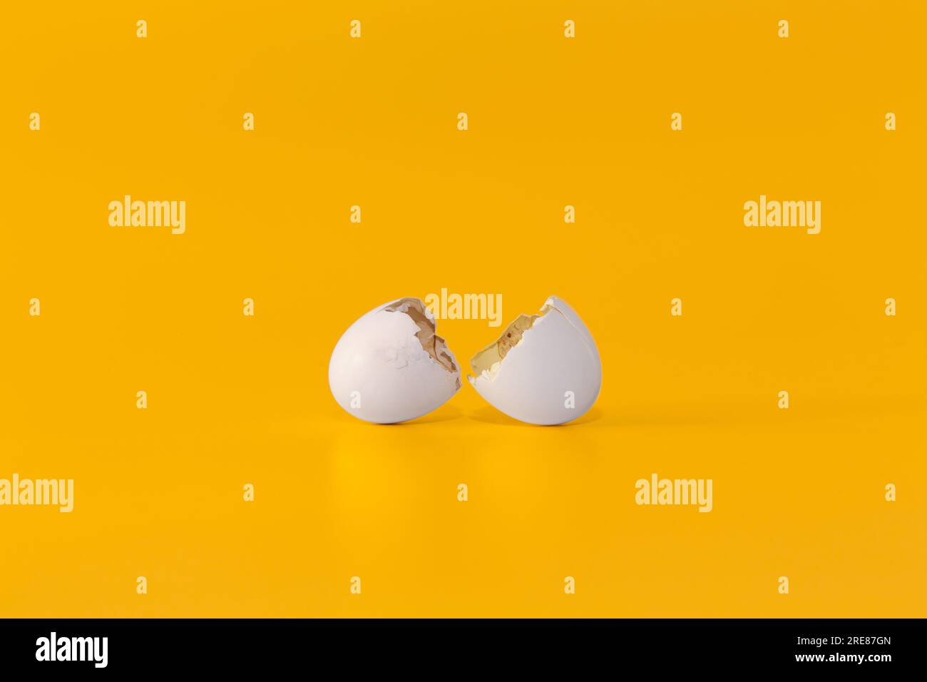 Broken white eggshell on a bright yellow background. Minimalist conceptual image of a cracked egg shell representing a new beginning or fragile life. Stock Photo