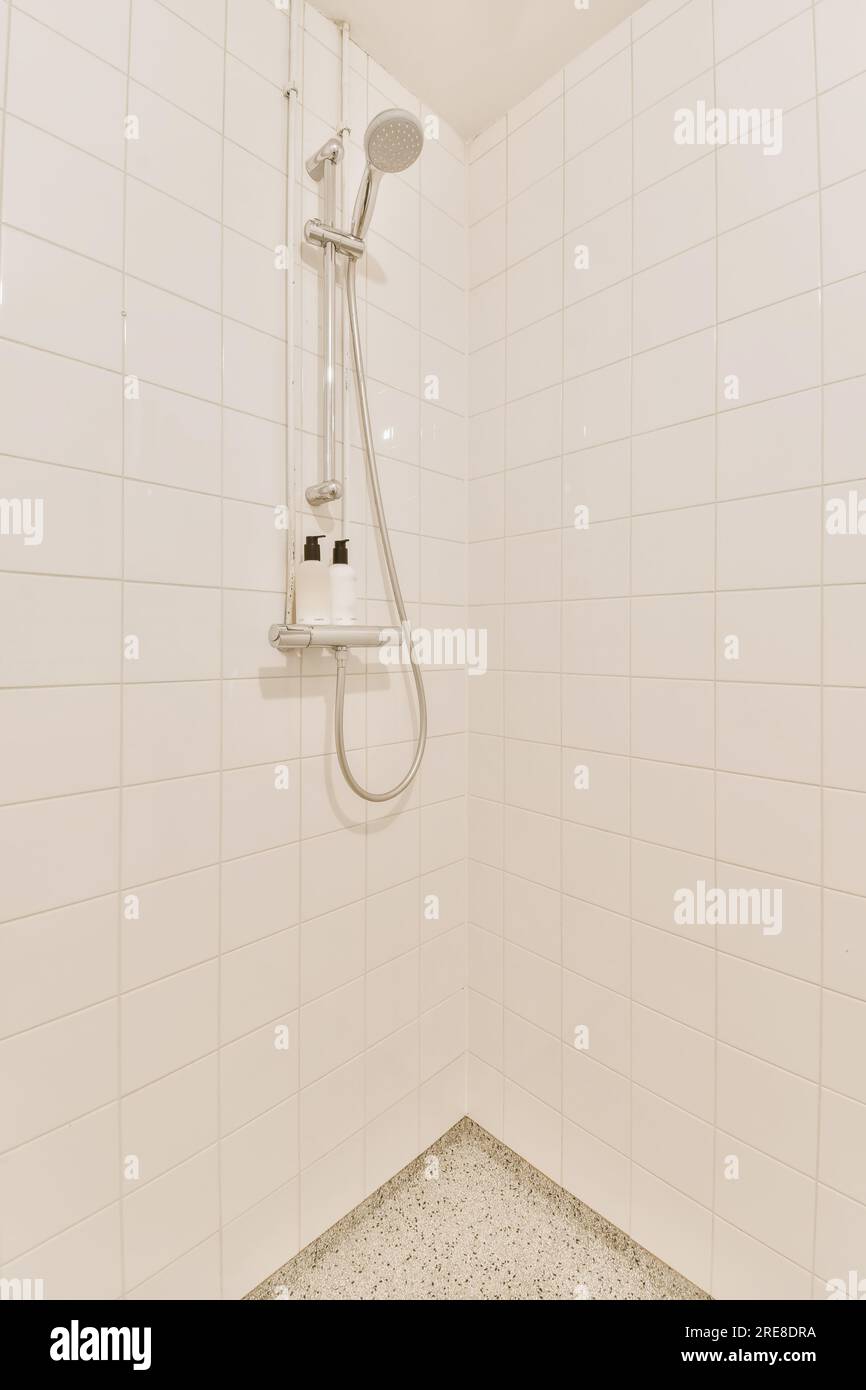 https://c8.alamy.com/comp/2RE8DRA/a-white-tiled-bathroom-with-shower-head-and-hand-held-in-the-shower-arm-which-is-connected-to-the-wall-2RE8DRA.jpg