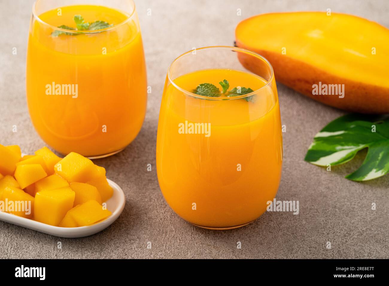 Fresh beautiful delicious mango juice. Close up design concept of smoothie cold drink in glass cup with glass straw on gray table background. Stock Photo
