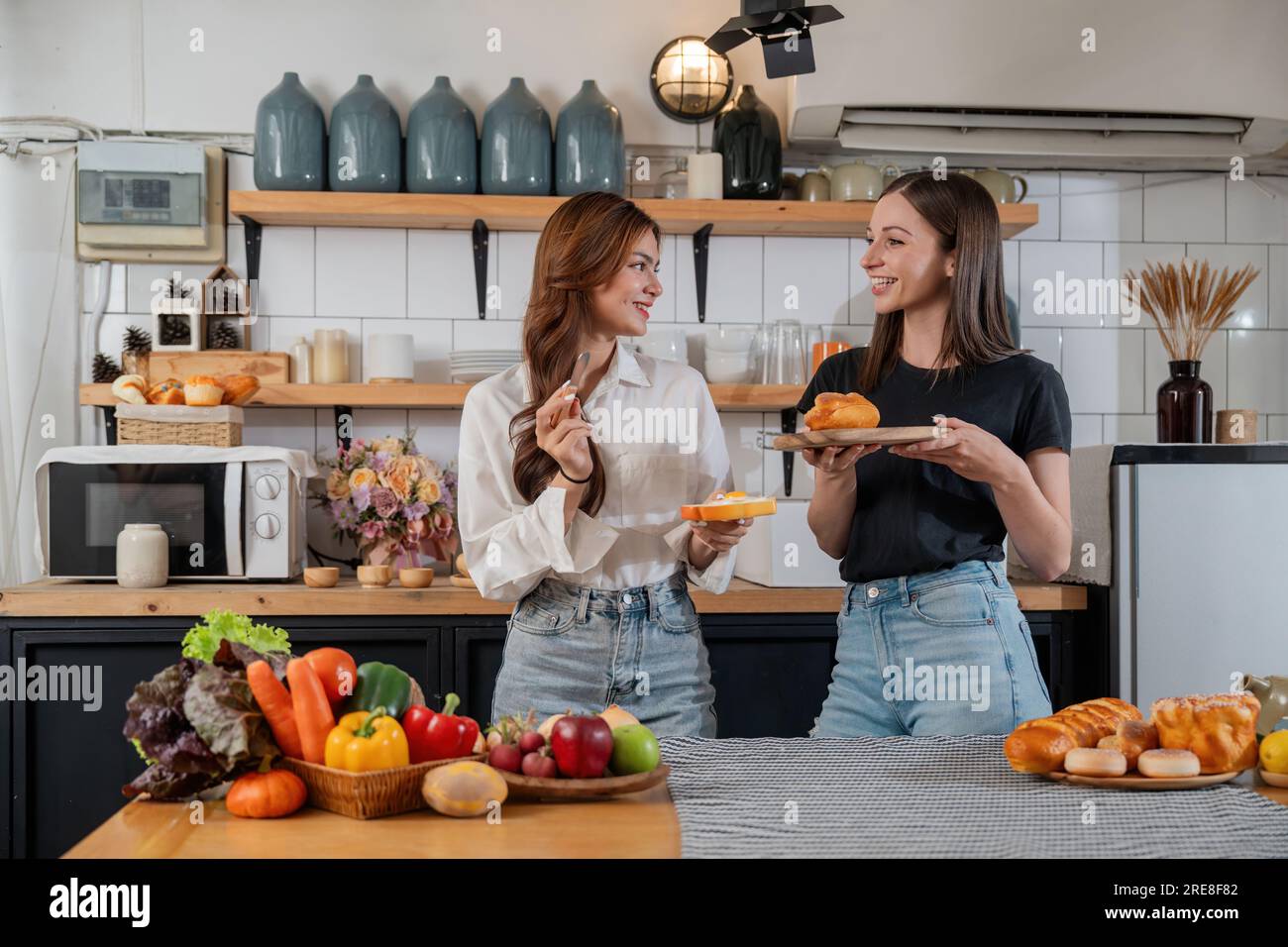 Two beautiful woman friends enjoy breakfast in kitchen drinking coffee