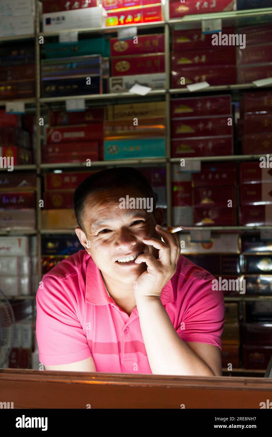 Young male shop assistant man and display of cigarettes and other