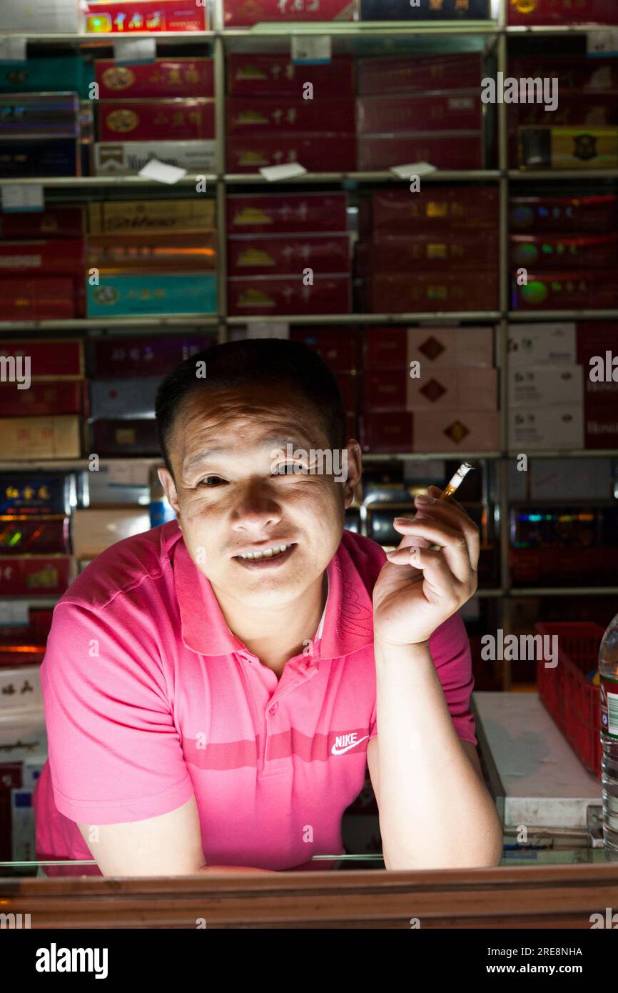 Young male shop assistant man and display of cigarettes and other