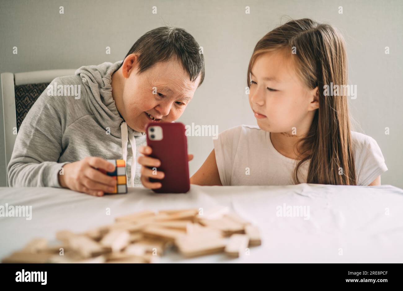 Young girl's heartwarming assistance empowers elderly woman with Down syndrome to make phone calls Stock Photo