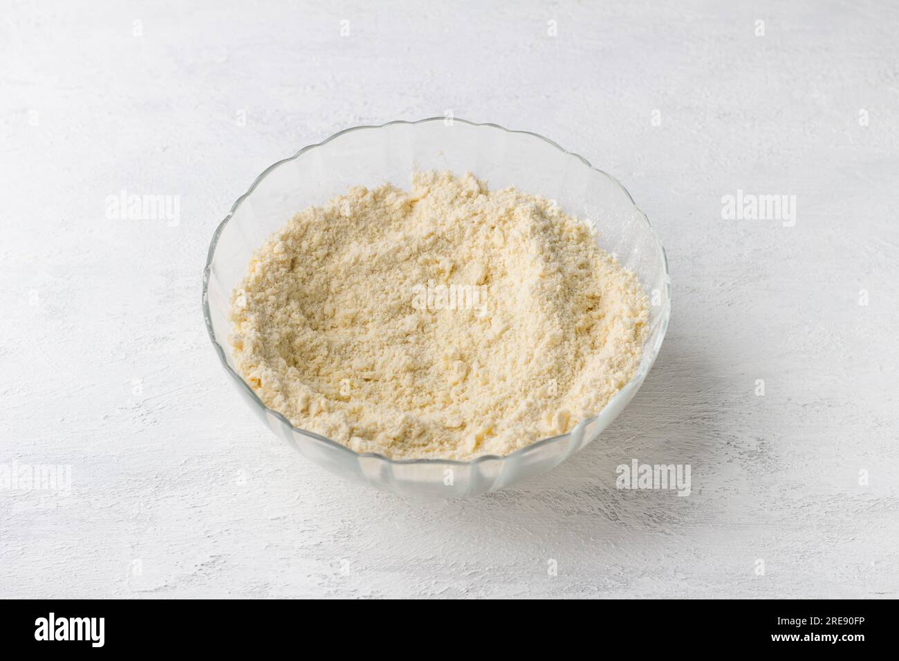 A glass bowl of grated butter with flour on a light gray background. Cooking delicious homemade pastries, step by step, cooking step. Stock Photo