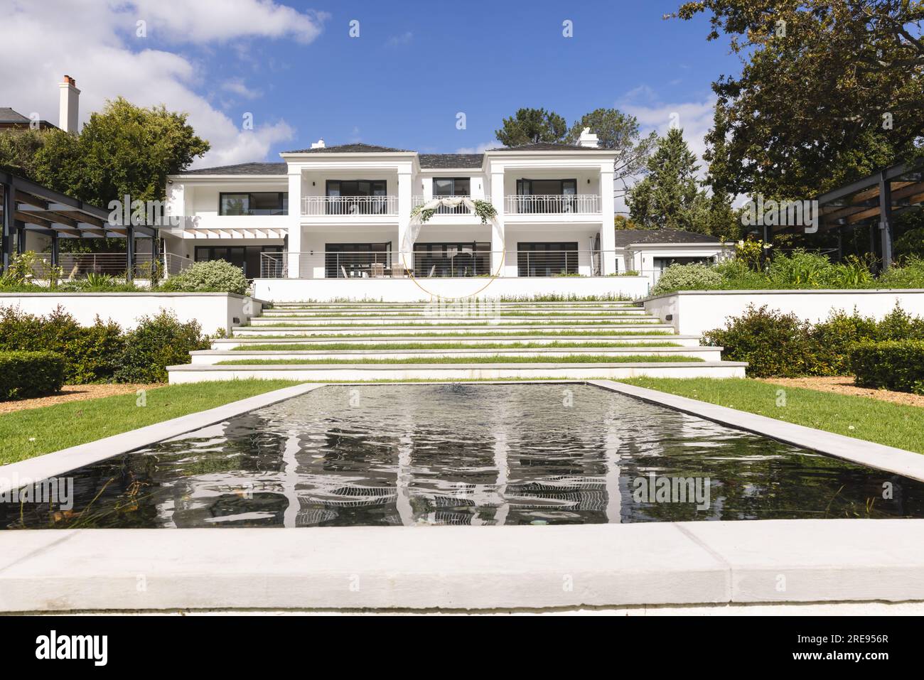 Sunny garden with pond feature and steps up to large modern house, copy space Stock Photo