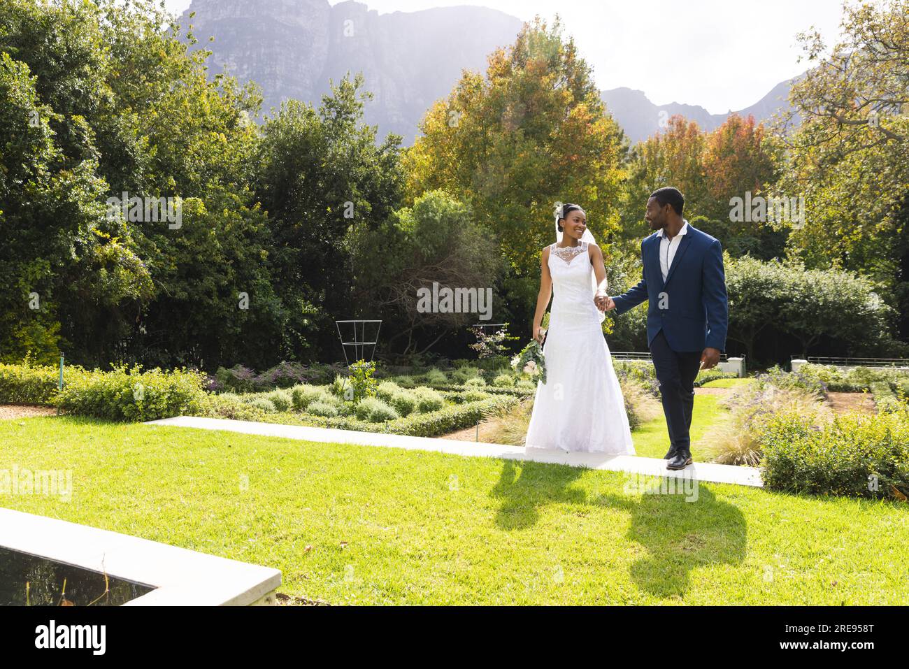 Happy african american bride and groom holding hands and walking in ...