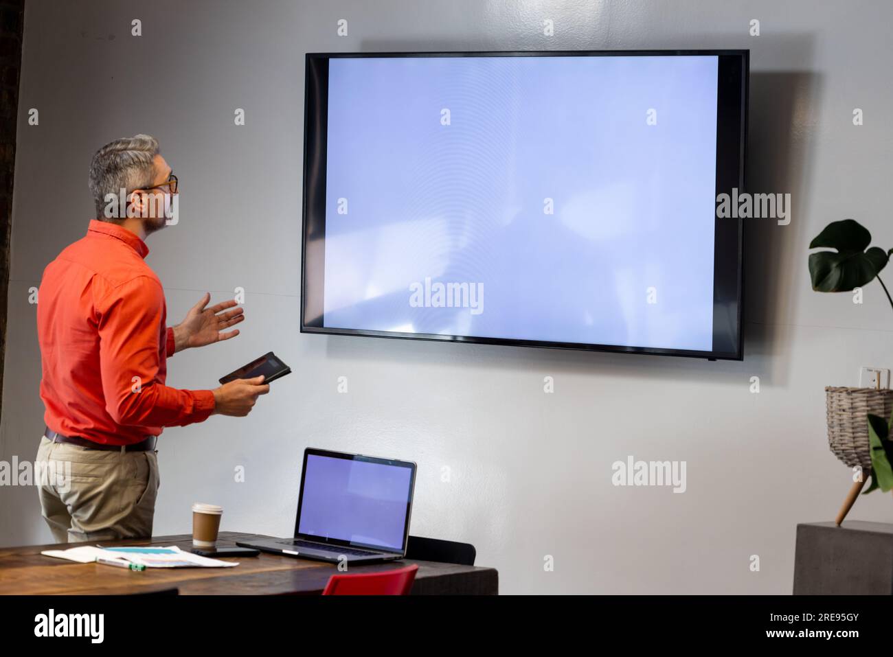 Caucasian businessman holding a digital tablet having a video call on tv with copy space at office Stock Photo