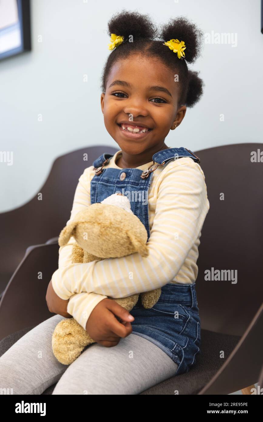 Portrait of african american girl patient holding teddy bear, sitting