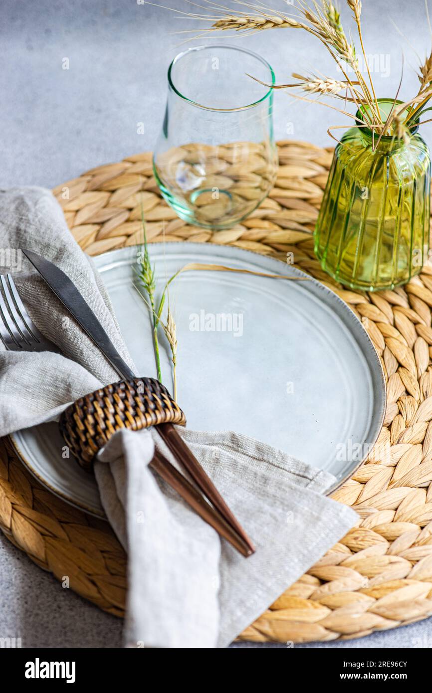 https://c8.alamy.com/comp/2RE96CY/from-above-an-elegant-white-ceramic-plate-with-napkin-wrapped-cutlery-placed-on-a-straw-accent-and-a-glass-vase-with-ears-of-dried-wheat-2RE96CY.jpg