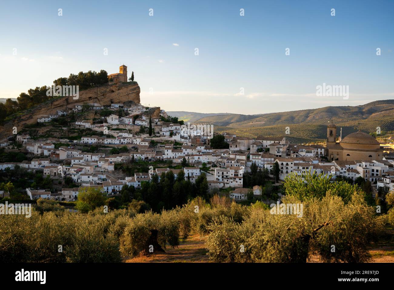 Picturesque view of aged town on hill with stone buildings and green trees under cloudless sky in n Montefrio village, Pueblos Blancos in Spain Stock Photo