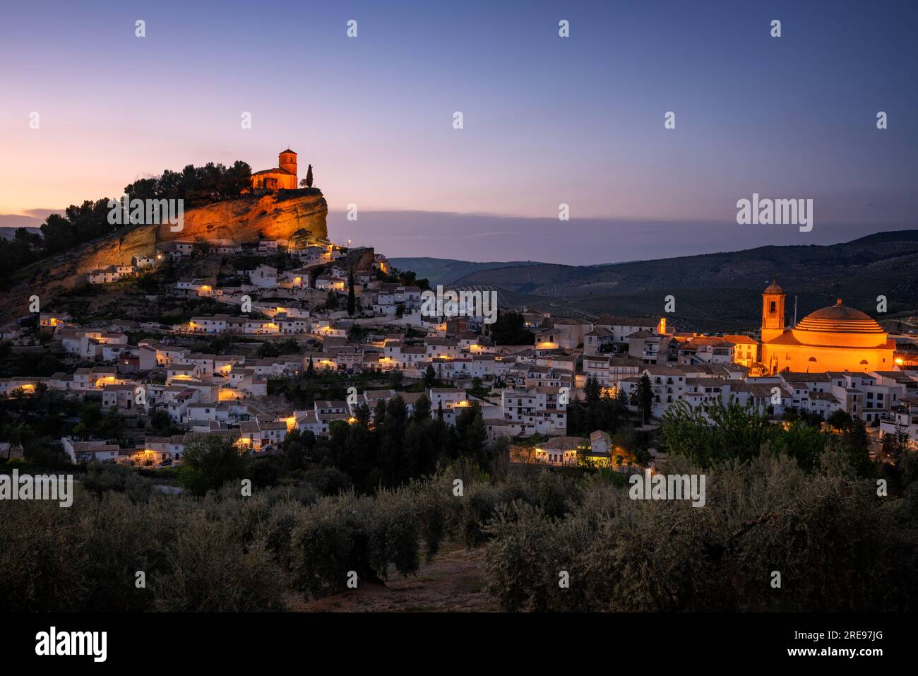 Picturesque view of aged town on hill with stone buildings and green trees under cloudless sky at sunset in n Montefrio village, Pueblos Blancos in Sp Stock Photo