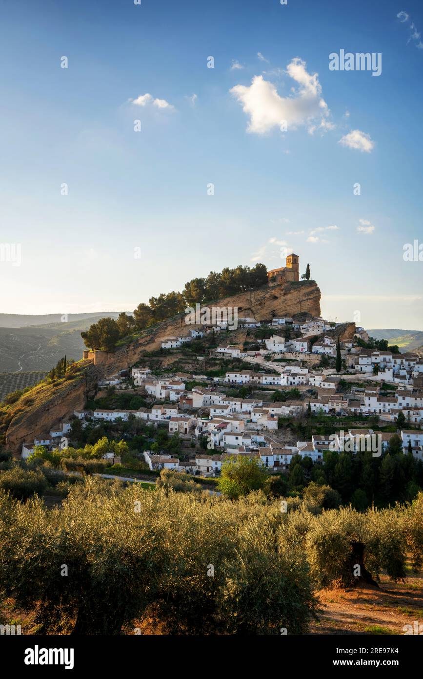 Picturesque view of aged town on hill with stone buildings and green trees under cloudless sky in n Montefrio village, Pueblos Blancos in Spain Stock Photo