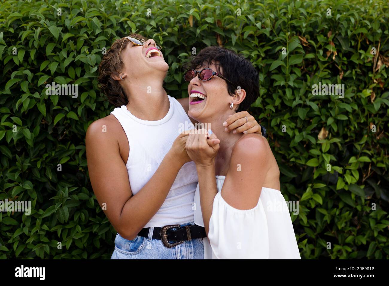 Adult friendly women cuddling in green park while smiling sincerely