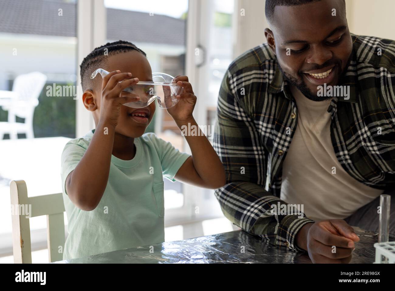 Happy african american father and son doing chemistry experiment together in sunny living room Stock Photo