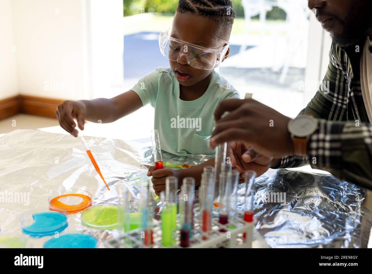Happy african american father and son doing chemistry experiment together in sunny living room Stock Photo
