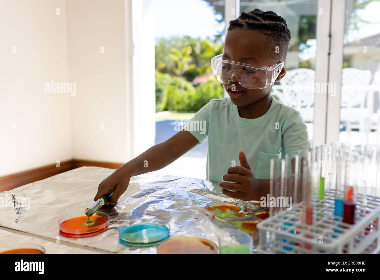 Happy african american boy doing chemistry experiments at home in sunny living room Stock Photo