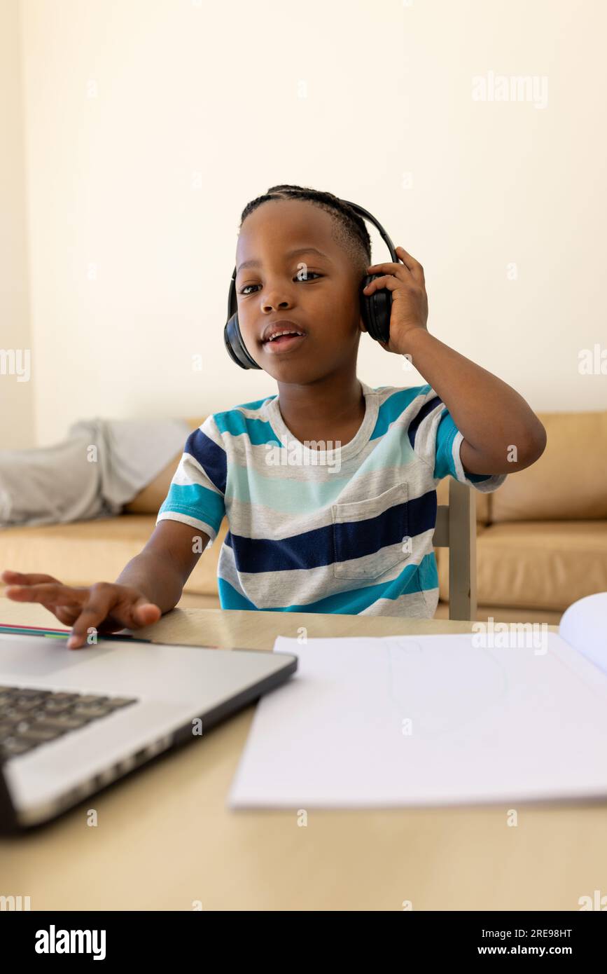 Happy african american boy sitting table using laptop and headphones in