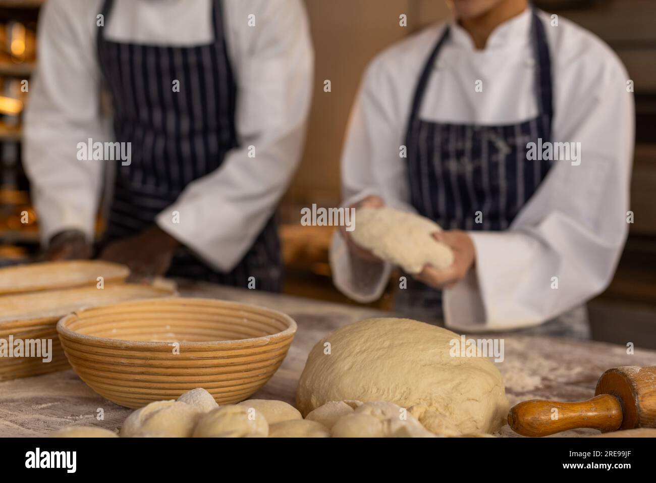 Diverse bakers wearing aprons in bakery kitchen and holding dough. Food